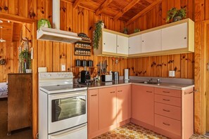 A kitchen with wooden walls, a stove, cabinets, and a sink. - Rotoiti Boathouse - Waterfront, Jetty, Kayaks (Rotoiti Forest)