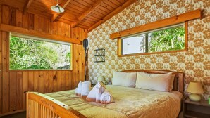 Una habitación de madera con una cama, dos ventanas y una lámpara.