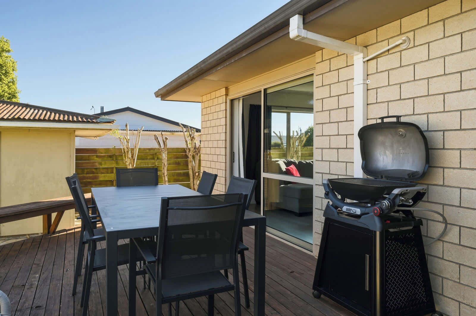 An outdoor patio with a table and chairs, a barbecue grill, and a glass door leading to a covered area.