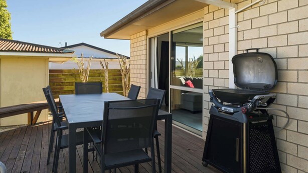 Un patio exterior con mesa y sillas, una parrilla y una puerta de cristal que da a un área cubierta.