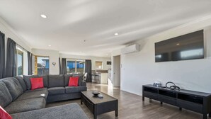 Una sala de estar moderna con un sofá modular, una mesa de centro, un televisor y una cocina al fondo.