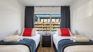 Habitación de hotel con dos camas, una mesita de noche y una ventana con vista a una terraza de madera.