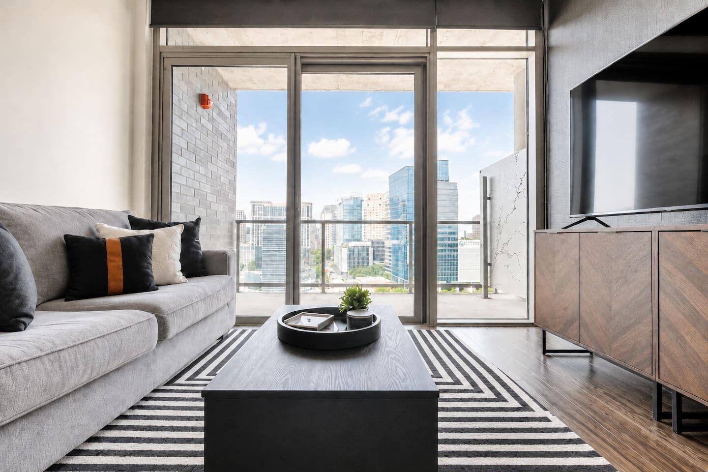 A modern living room with a sofa, coffee table, and a view of the cityscape through large windows.
