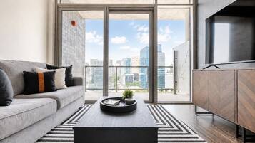 A modern living room with a sofa, coffee table, and a view of the cityscape through large windows.