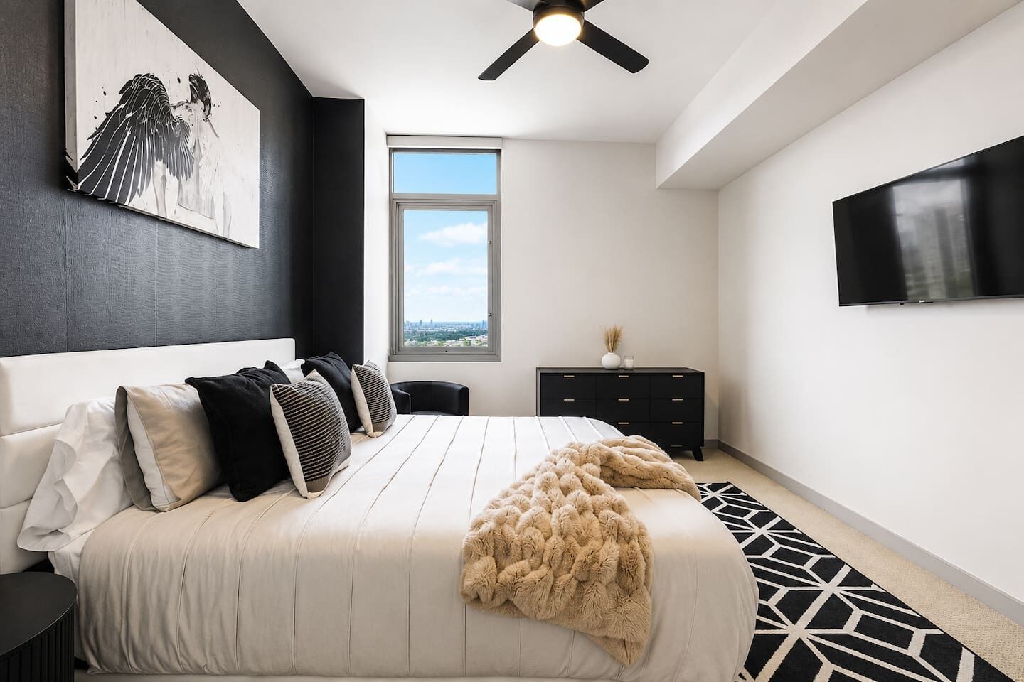 A modern bedroom with a bed, a ceiling fan, a window, a TV, and a city view.