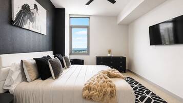 A modern bedroom with a bed, a ceiling fan, a window, a TV, and a city view.