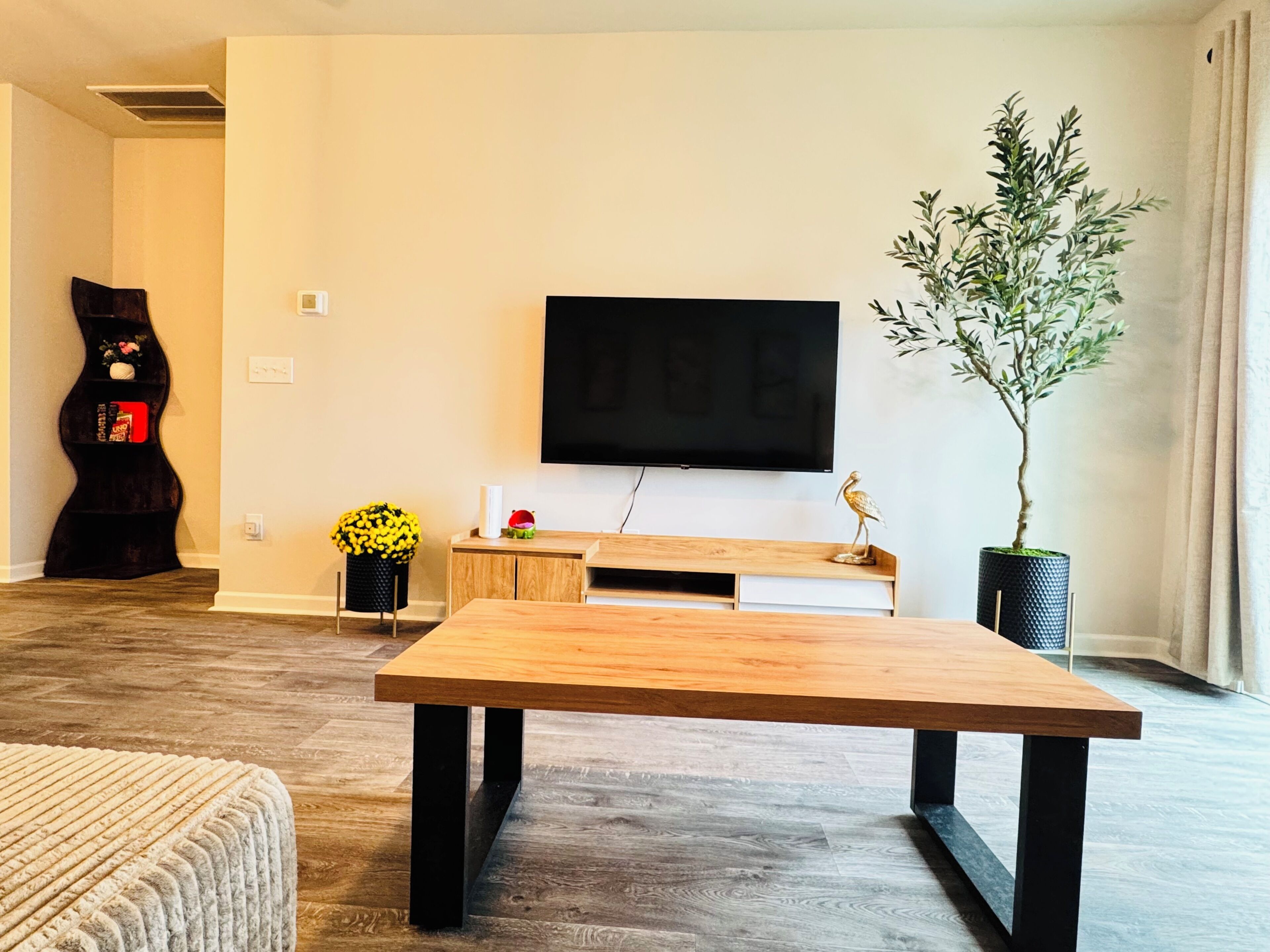 Een woonkamer met een houten salontafel, een flatscreen televisie aan de muur, een potplant en een decoratieve plank.