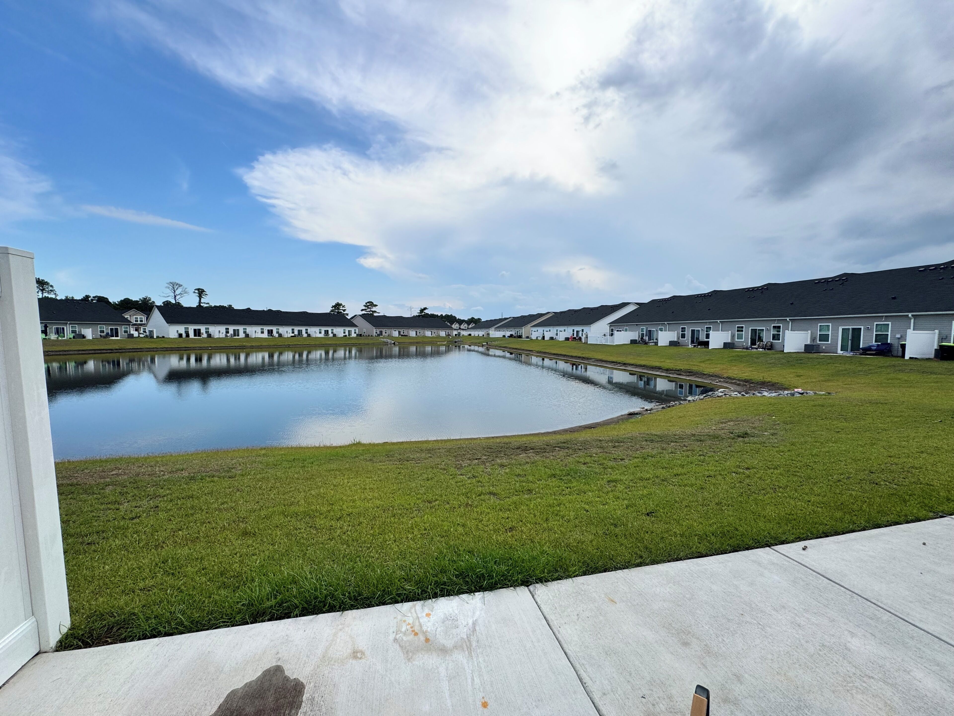 A residential area with a large pond, houses with uniform architecture, and a clear sky.