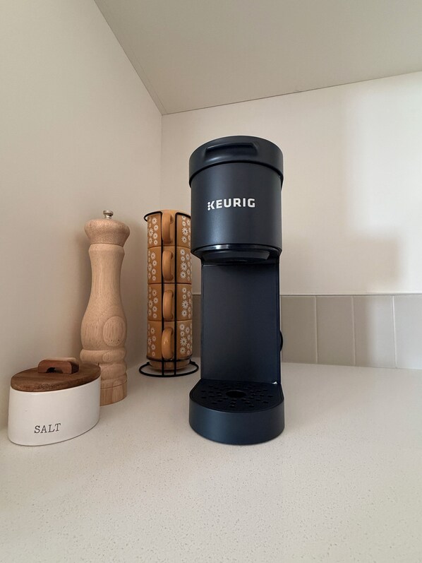 Un comptoir de cuisine avec une machine à café Keurig noire, un salier en bois et un joli récipient à sel décoratif.