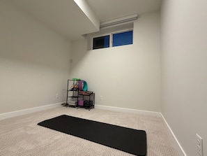 A room with a black exercise mat, a small shelf with various items, and a window with blue blinds. - Rockies Retreat (Calgary)