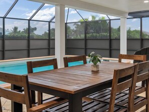 Ein Holztisch mit Stühlen und einem Topfpflanzen, vor einem Blick auf einen Pool mit Glasveranda.
