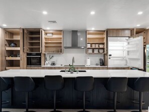 A modern kitchen with a central island, bar stools, and open cabinets. - Waterfront retreat with heated pool and private dock! (Port Charlotte)