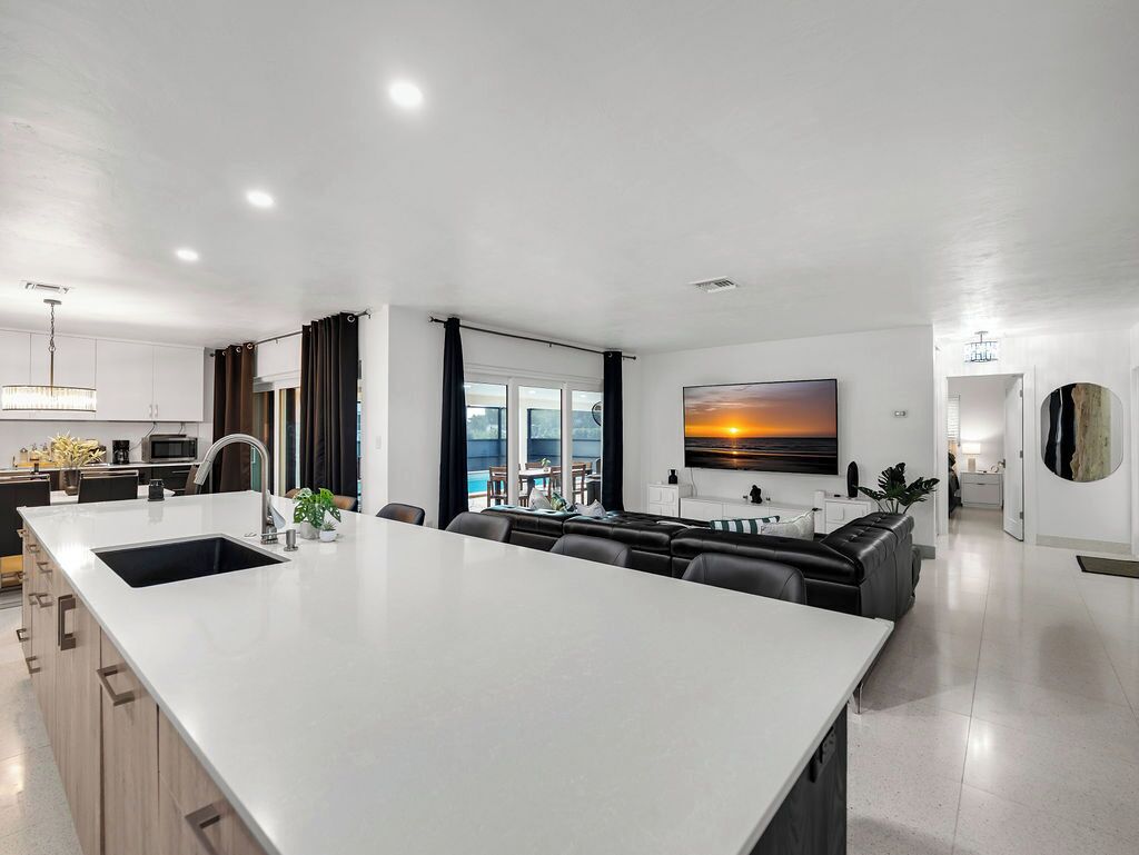 A modern kitchen with a large island, dining area with a view, and a living space with a large painting.