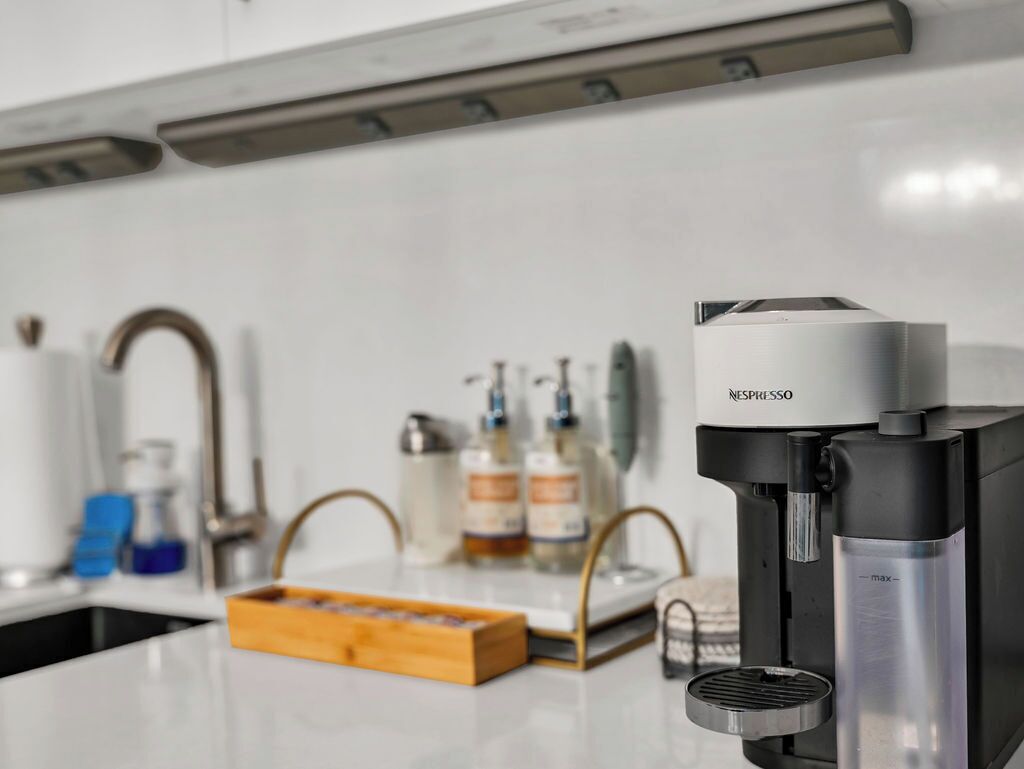 Uma cozinha moderna com uma cafeteira Nespresso, uma pia e um balcão com uma caixa de cápsulas de café.