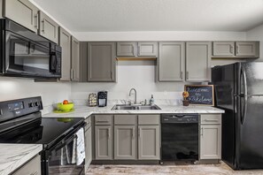 Eine moderne Küche mit grauen Schränken, einem schwarzen Kühlschrank, einem eingebauten Backofen, einer Mikrowelle und einem Geschirrspüler.