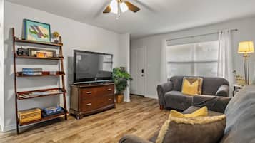 Ein Wohnzimmer mit Fernseher, Holzregalen, einer Couch und einem Deckenventilator.