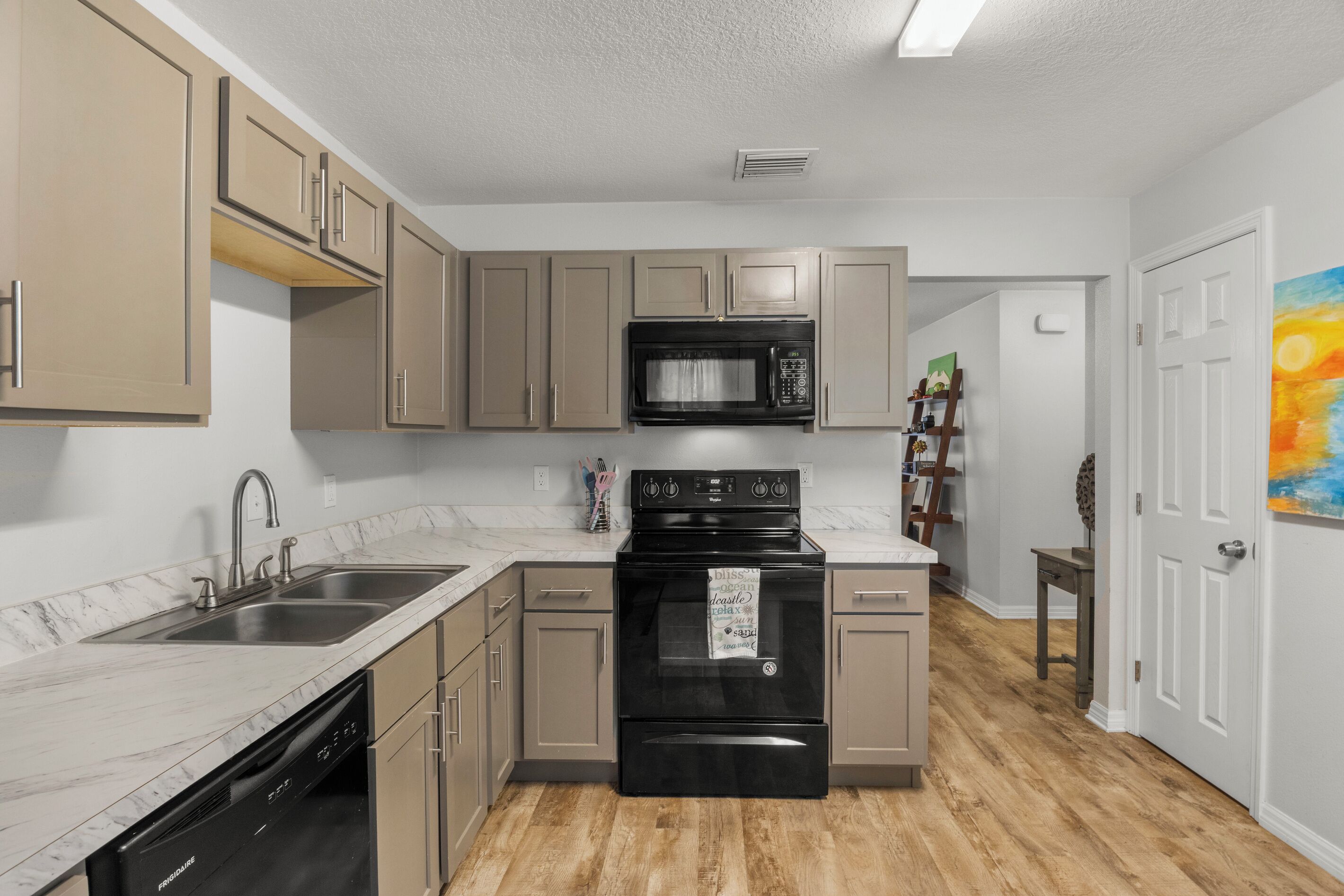 Una cocina con gabinetes color beige, un microondas negro, una estufa negra y un lavavajillas.
