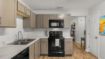 Una cocina con gabinetes color beige, un microondas negro, una estufa negra y un lavavajillas.