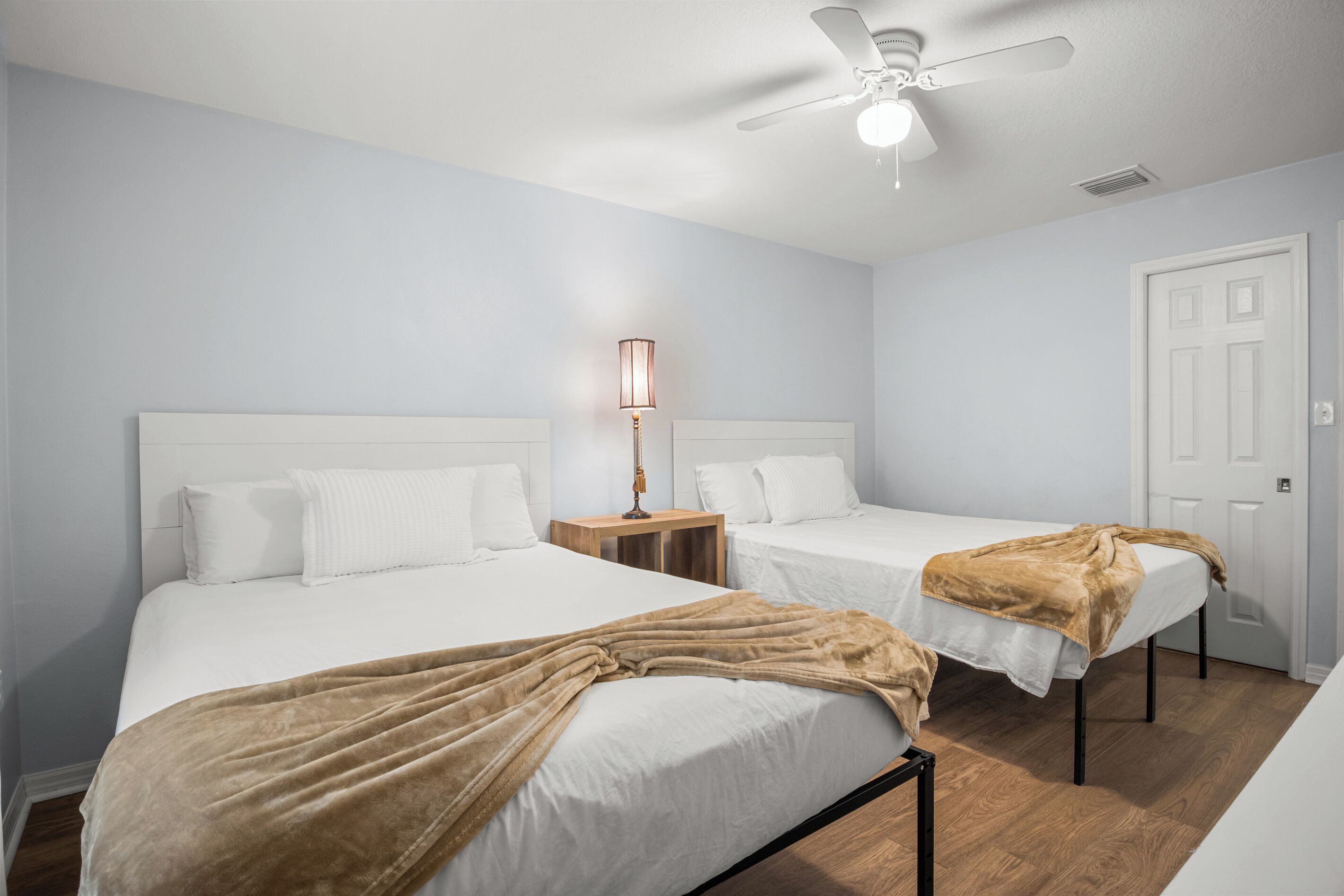 Une chambre d’hôtel avec deux lits, un ventilateur de plafond, une table de chevet avec une lampe et une porte.