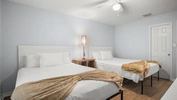 A hotel room with two beds, a ceiling fan, a bedside table with a lamp, and a door.