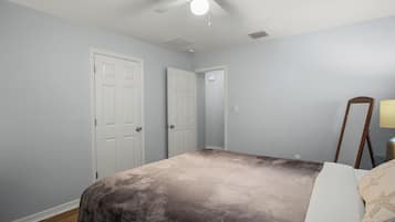 Un dormitorio con cama, ventilador de techo, dos puertas blancas y una mesita de noche con lámpara.