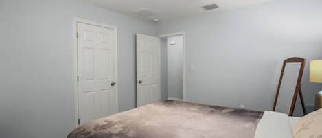 A bedroom with a bed, a ceiling fan, two white doors, and a nightstand with a lamp.
