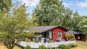 Ein rotes Haus mit weißem Zaun, einem Grillbereich und einem kleinen Garten mit Vogeltränke.