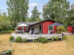 Una casa roja con valla de piquete blanca, mobiliario exterior y jardín.
