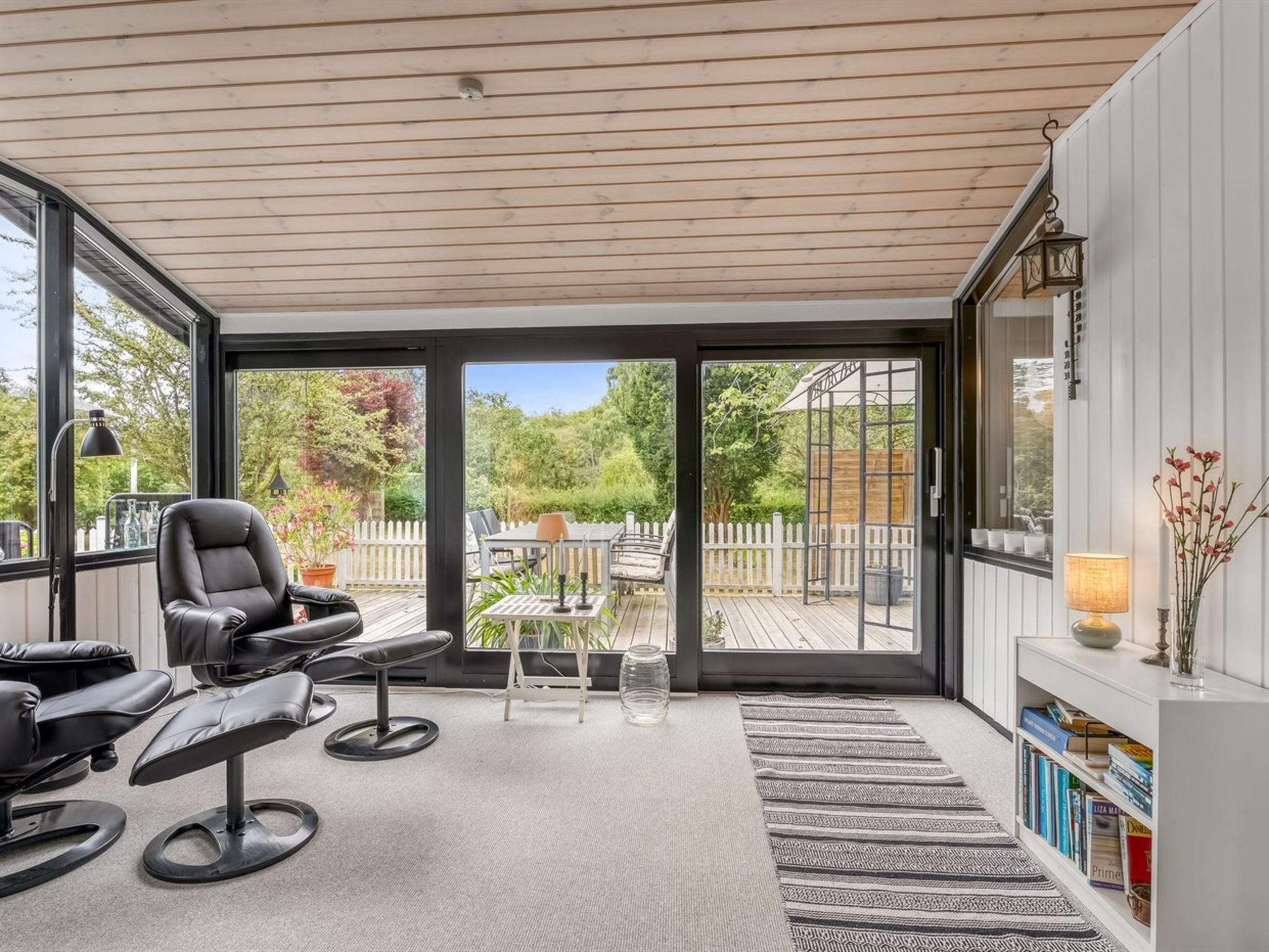 A modern interior with a glass door leading to an outdoor deck, a leather chair, a small table, and a bookshelf.
