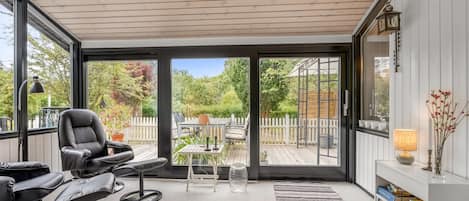 A modern interior with a glass door leading to an outdoor deck, a leather chair, a small table, and a bookshelf.
