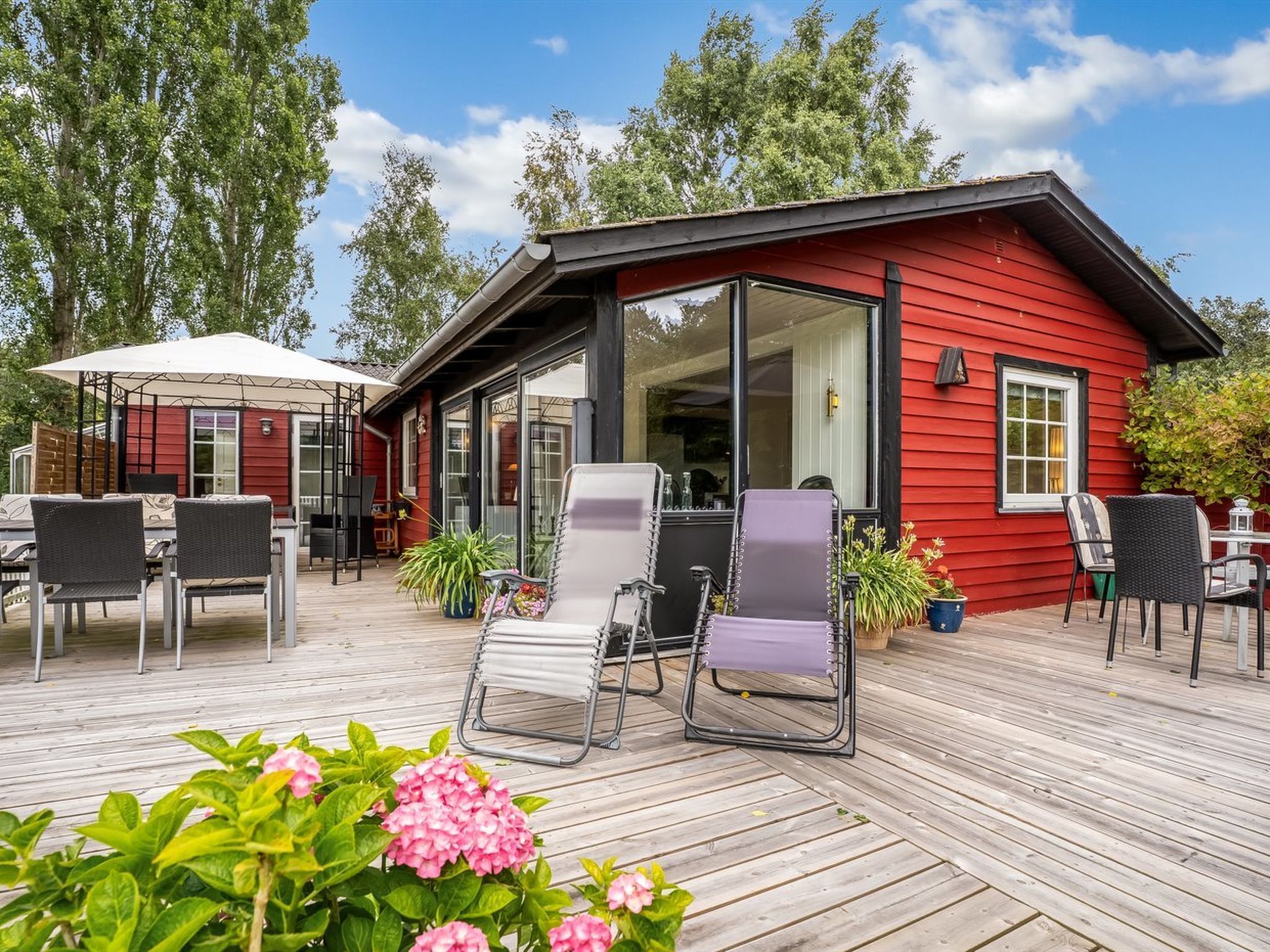 A red wooden building with a covered patio area, outdoor seating, and potted plants.