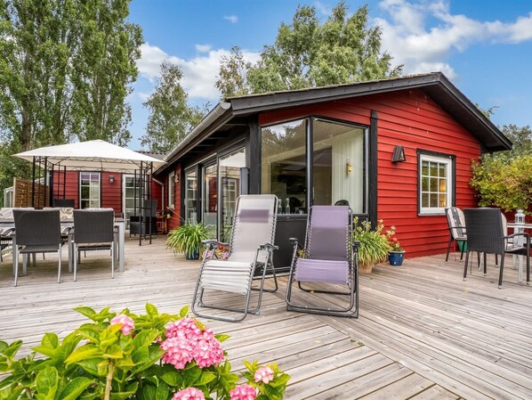 A red wooden building with a covered patio area, outdoor seating, and potted plants.