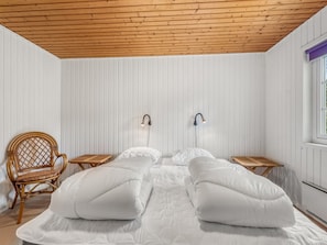 A room with a bed, two bedside tables, a chair, and a window.