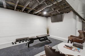 Een sportschool met een bank, halters, een televisie en een leren stoel.