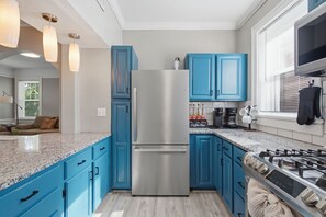 Eine moderne Küche mit blauen Schränken, einem Edelstahl-Kühlschrank, einem Gasherd und einer Kaffeestation.