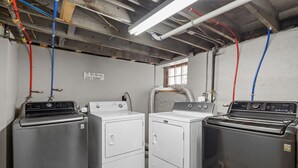 A laundry room with three stacked washers and dryers, exposed pipes, and a sign that says "Dirty Again". - Bright Upper-Level 3BR Near WashU & Forest Park (St. Louis)