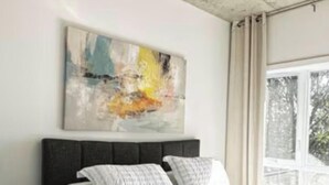 A bedroom with a bed, a nightstand, a painting on the wall, and a window with curtains. - Spacious 3 1/2-bedroom condo in Montreal (Montréal)