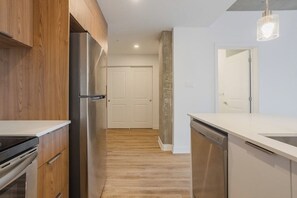 A modern kitchen with wooden cabinets, stainless steel appliances, and a white countertop. - Spacious 3 1/2-room apartment in Montreal (Montréal)