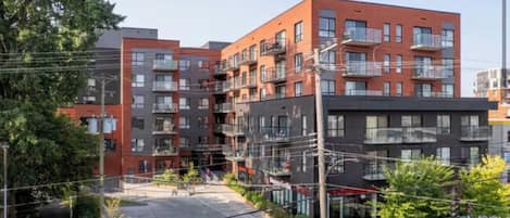 A multi-story residential building with balconies, a parking area, and a visible entrance.