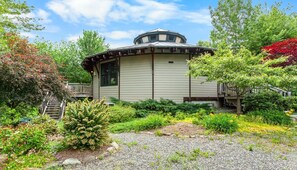 A building with a round tower, surrounded by a garden with various plants and a wooden deck. - Cranberry Cottage - NEW! Home in Trenton (Trenton)