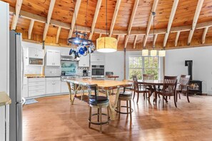 A spacious kitchen with wooden beams, a large island, and a dining area with chairs and a table. - Cranberry Cottage - NEW! Home in Trenton (Trenton)