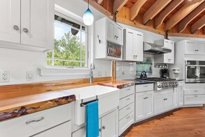 A modern kitchen with white cabinetry, a wooden countertop, a stove, and a window with a view of greenery. - Cranberry Cottage - NEW! Home in Trenton (Trenton)