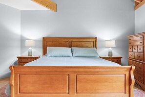 A wooden bed with two pillows, flanked by nightstands with lamps, in a room with a dresser and a sloped ceiling. - Cranberry Cottage - NEW! Home in Trenton (Trenton)