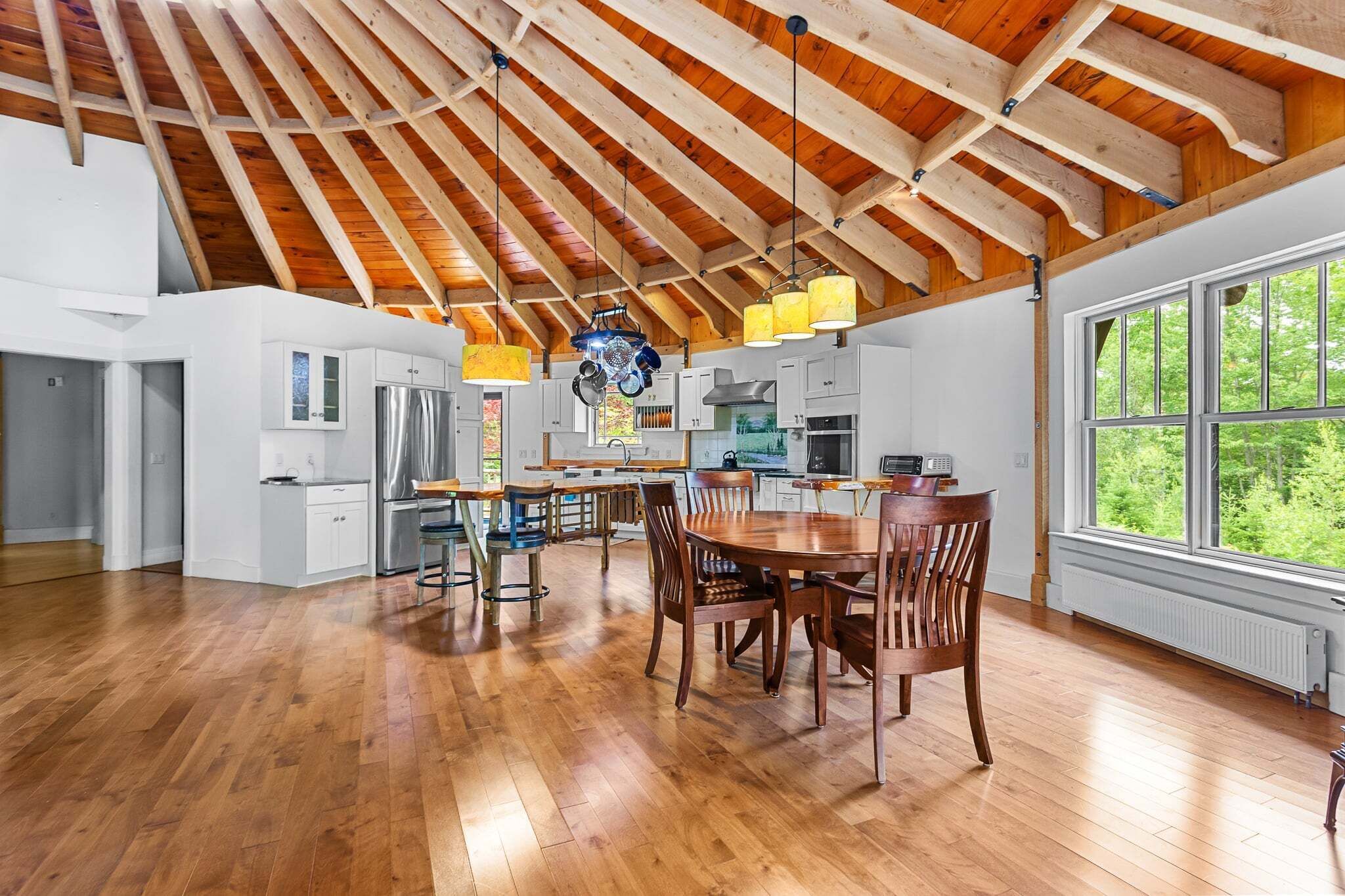 A spacious kitchen with wooden beams, a dining area with a large table and chairs, and a view of greenery through the windows.