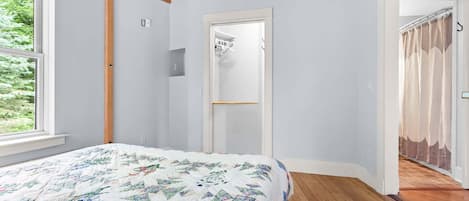 A bedroom with a bed, wooden beams, a door, and a view through a window.