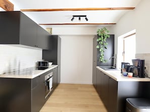 A modern kitchen with black cabinets, a white countertop, a built-in oven, a coffee maker, and a hanging plant. - Intimate village house with a rural location. (Palenge)