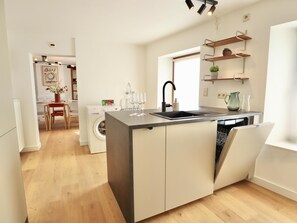 A modern kitchen with a central island, a washing machine, and a dining area with chairs and a table. - Renovated, intimate rural village house (Palenge)