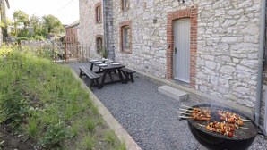 En byggnad av sten med en grill och picknickbord.