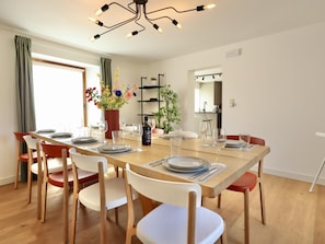 A dining area with a wooden table set for six, surrounded by chairs, a vase of flowers, and a modern light fixture. - Renovated, intimate rural village house (Palenge)