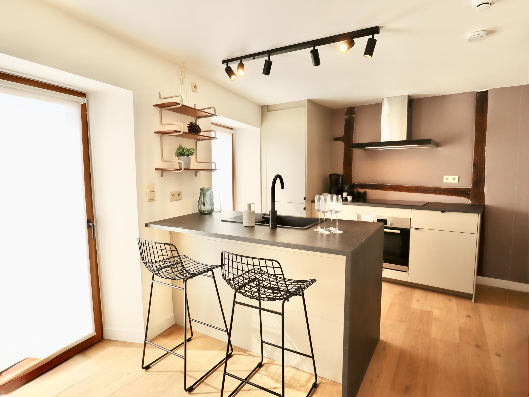Een moderne keuken met een centraal eiland, twee barkrukken, een inbouwoven en een hanglamp.